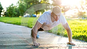 A young athletic man does push-ups. A muscular and strong guy is training. In nature in the park in the summer. Strength