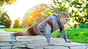 A young athletic man does push-ups. A muscular and strong guy is training. In nature in the park in the summer. Strength