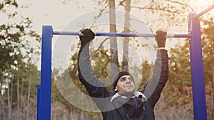 Young athletic man doing pull-up exercise in winter park outdoors