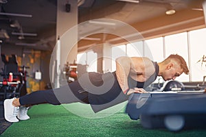 Young athletic man doing push-ups in gym. Muscular and strong guy exercising.