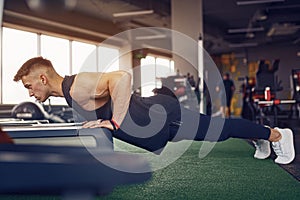 Young athletic man doing push-ups in gym. Muscular and strong guy exercising.