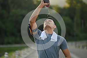 Young athletic man drinking water from a bottle, taking a break from workout in the park.