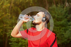 Young athletic man drinking water outdoors in the park