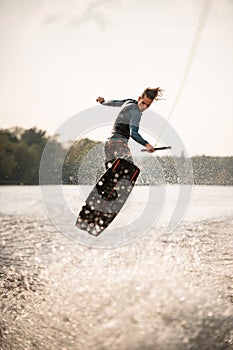 young athletic man jumps spectacularly on wakeboard above the water with splashes