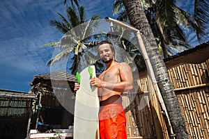 Young athletic man with kite surfing board desalinates the board under the shower on beach on summer vacation