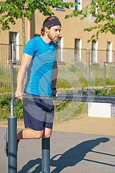 Young athletic man pulling up on parallel metal bars while working out on stadium