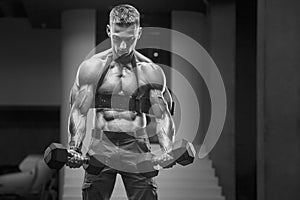 Young athletic man pumping up muscles in the gym at workout