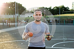 Young athletic man in a t-shirt holds a Burger and an Apple in the background of the stadium