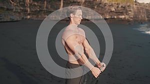 Young athletic man trains his biceps and triceps at the sandy beach close up.