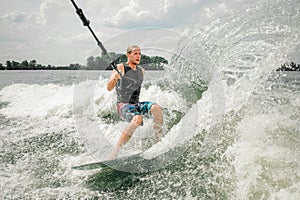 Young athletic man wakesurfing on the board holding a cable