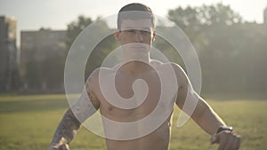 Young athletic man warming up in sunlight outdoors. Portrait of confident handsome Caucasian man exercising at sunrise