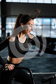 Young Athletic middle aged woman training on air resistance bike, cross training workout set in gym. Active woman spinning a air