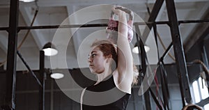 Young athletic red haired professional athlete woman lifting kettlebell weight in large atmospheric gym slow motion.