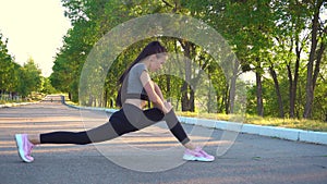 Young athletic woman in black sportswear does stretching exercises outdoor.
