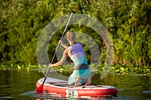 Young athletic woman doing fitness on a board with an oar on a lake.