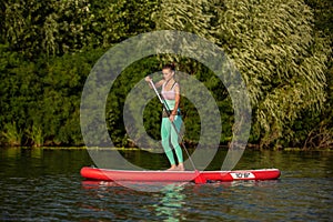 Young athletic woman doing fitness on a board with an oar on a lake.