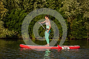 Young athletic woman doing fitness on a board with an oar on a lake.