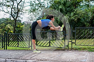 Young athletic woman doing warming-up exercises, stretching her legs on fence at road before running