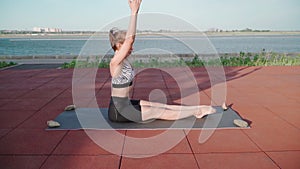 Young Athletic Woman Doing Yoga on a Lake Background. Beautiful Girl Is Exercising Outdoors. Stretching Exercises and Flexibility