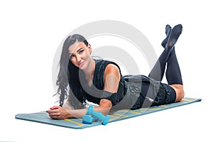 A young athletic woman in an EMS suit does lies on a Mat with dumbbells on an isolated white background. EMS training