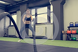 Young athletic woman exercising in gym using battle rope.
