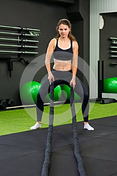 Young athletic woman exercising in gym using battle rope.