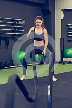 Young athletic woman exercising in gym using battle rope.