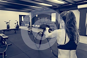 Young athletic woman exercising in gym using battle rope.