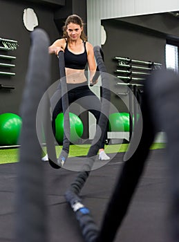 Young athletic woman exercising in gym using battle rope.