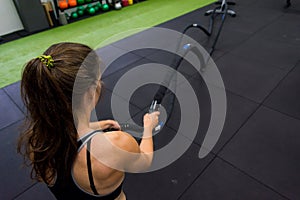 Young athletic woman exercising in gym using battle rope.