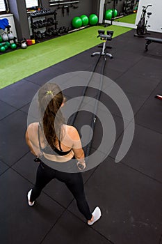 Young athletic woman exercising in gym using battle rope.