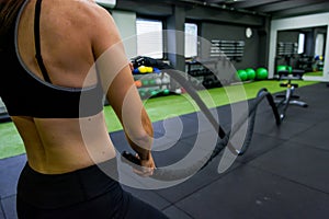 Young athletic woman exercising in gym using battle rope.