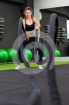 Young athletic woman exercising in gym using battle rope.