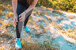 A young athletic woman is experiencing pain in her leg due to an injury while Jogging on rough terrain. Concept of sports and