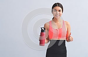 Young athletic woman in fitness equipment having a bottle of water in hand, on blue background