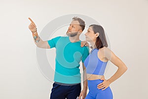 Young athletic woman and man in blue sportswear standing and pointing by finger, white background. Keeping fit by