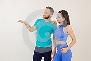 Young athletic woman and man in blue sportswear standing and pointing by hand, white background. Keeping fit by fitness