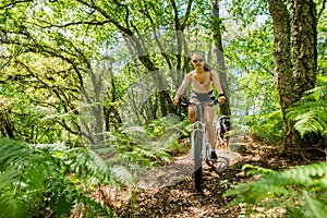 young athletic woman mountain biking with her dog in the forest of southwest France