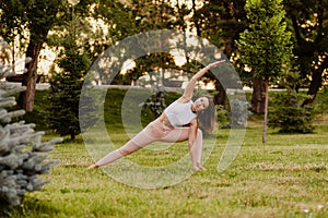 Young athletic woman practice yoga in green park on grass in summer morning. Stand in extended side angle pose in