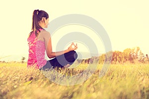 Young athletic woman practicing yoga on a meadow at sunset