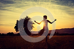 Young athletic woman practicing yoga on a meadow at sunset