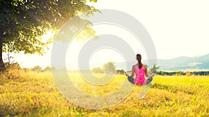 Young athletic woman practicing yoga on a meadow at sunset