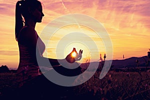Young athletic woman practicing yoga on a meadow at sunset