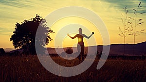 Young athletic woman practicing yoga on a meadow at sunset