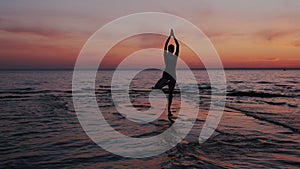 Young athletic woman standing alone and performing yoga tree pose. Seascape sunset, meditation, physical activity, gym