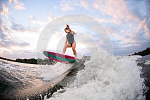 Young athletic woman on surf style wakeboard and balances on big splashing wave