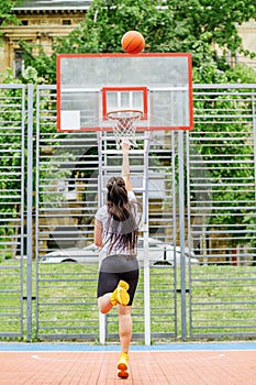 Young athletic woman is training to play basketball on modern outdoor basketball court