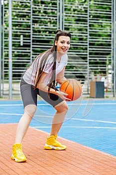 Young athletic woman is training to play basketball on modern outdoor basketball court. Happy woman