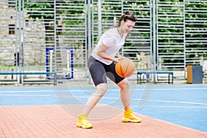 Young athletic woman is training to play basketball on modern outdoor basketball court. Happy woman