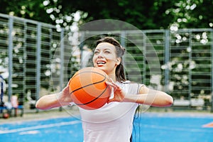 Young athletic woman is training to play basketball on modern outdoor basketball court. Happy woman